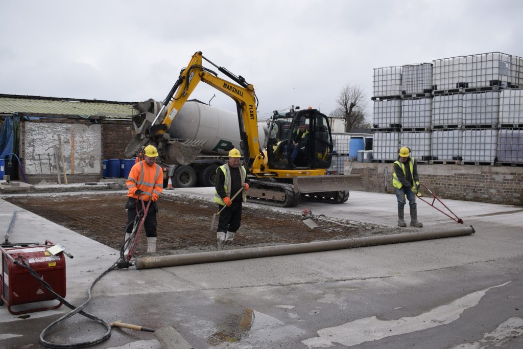 Concrete slab being laid by the site team, with excavator and concrete mixer